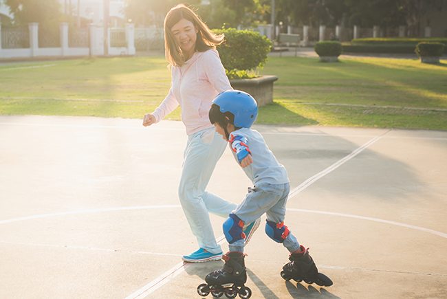 Young woman holding hand with boy rollerblading