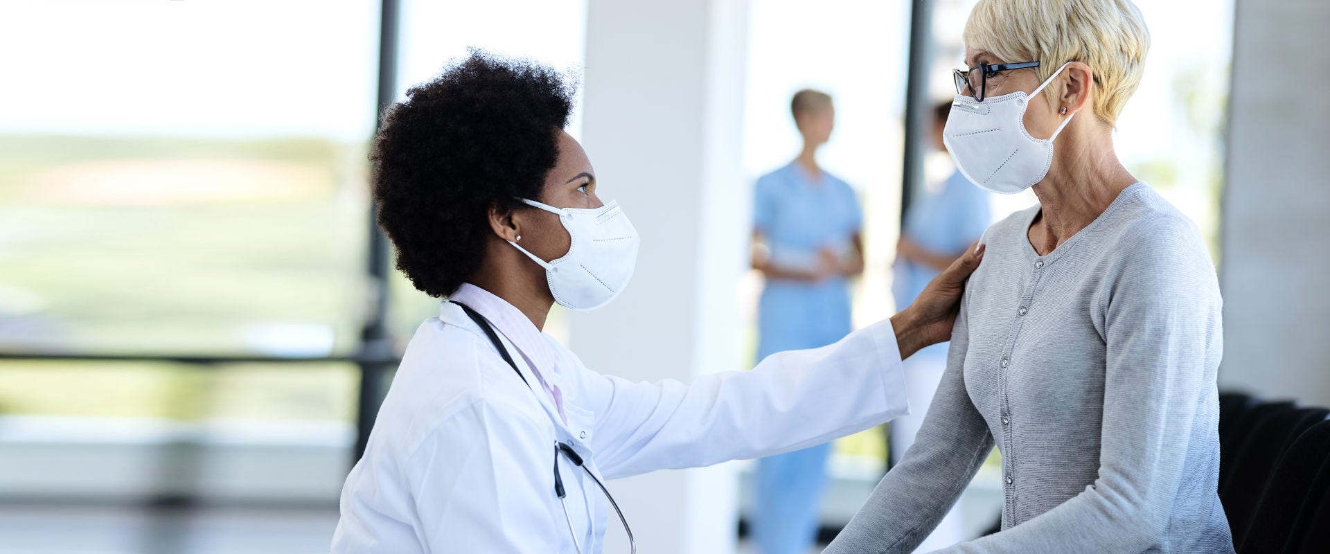 Healthcare professional consulting with a masked patient in a clinical setting.